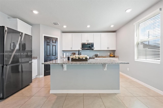 kitchen with an island with sink, white cabinetry, stainless steel appliances, and light stone counters