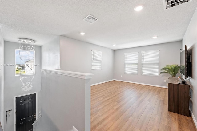 living room with a textured ceiling, light hardwood / wood-style floors, an inviting chandelier, and plenty of natural light