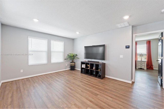 unfurnished living room featuring light wood-type flooring, a textured ceiling, and plenty of natural light