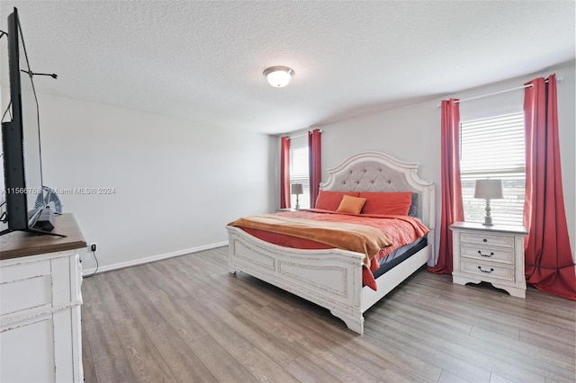 bedroom featuring a textured ceiling, light hardwood / wood-style floors, and multiple windows