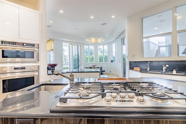 kitchen featuring sink, stainless steel double oven, backsplash, dark stone countertops, and white cabinets