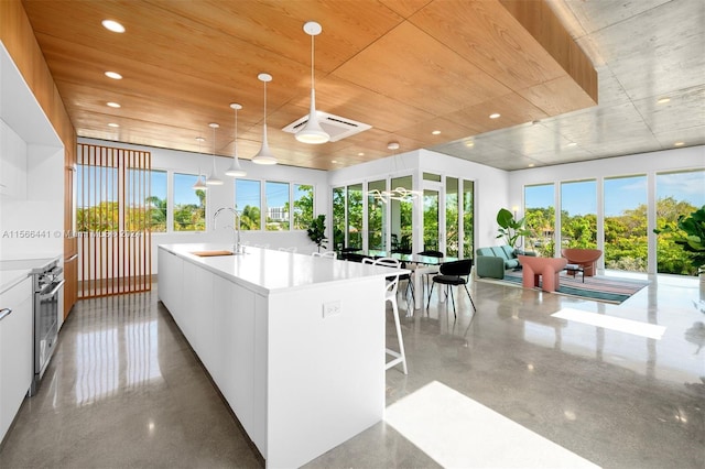 kitchen featuring stainless steel range with electric stovetop, sink, an island with sink, decorative light fixtures, and white cabinetry