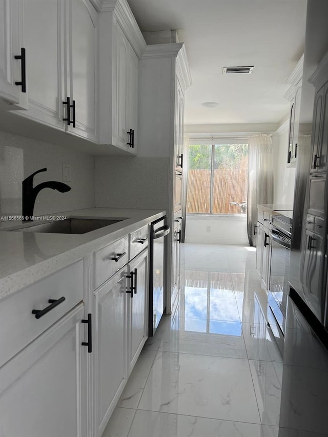 kitchen featuring oven, light stone counters, white cabinets, sink, and light tile floors