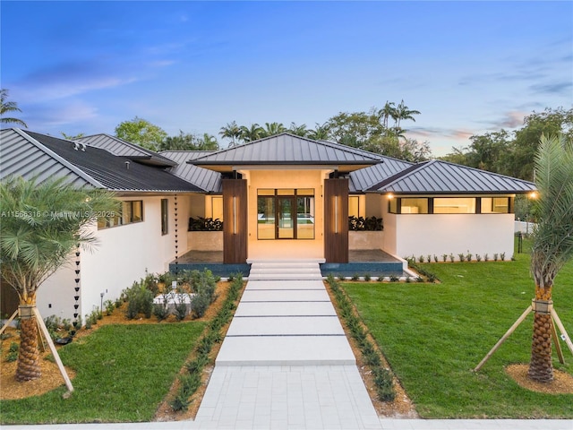 view of front of home with a standing seam roof, a lawn, and stucco siding