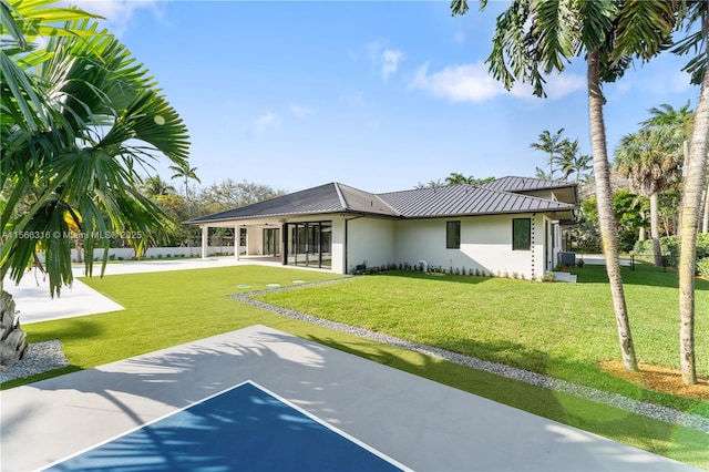 rear view of property featuring metal roof, a standing seam roof, fence, a yard, and stucco siding