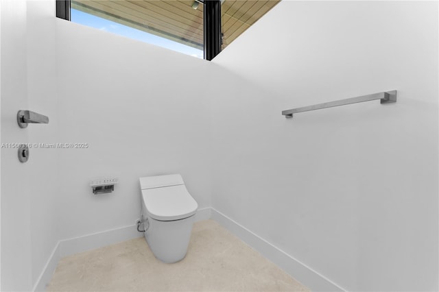 half bath featuring baseboards and toilet