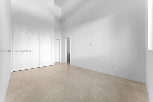 unfurnished bedroom featuring a closet, baseboards, and a high ceiling