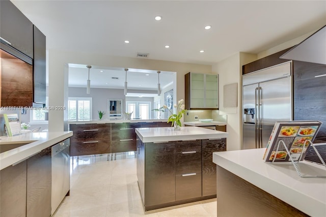 kitchen with appliances with stainless steel finishes, a kitchen island, light tile floors, and decorative light fixtures