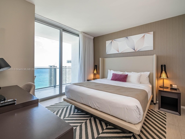 bedroom featuring access to exterior, a wall of windows, a water view, and light wood-type flooring