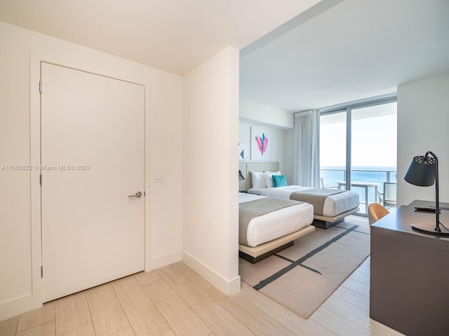 bedroom with floor to ceiling windows, a water view, light wood-type flooring, and access to exterior