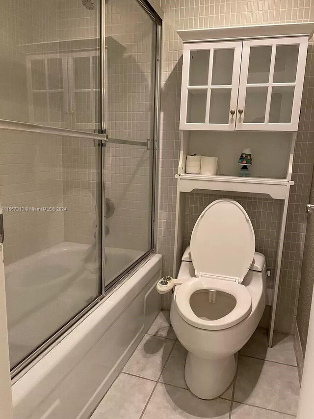 bathroom featuring combined bath / shower with glass door, toilet, and tile floors