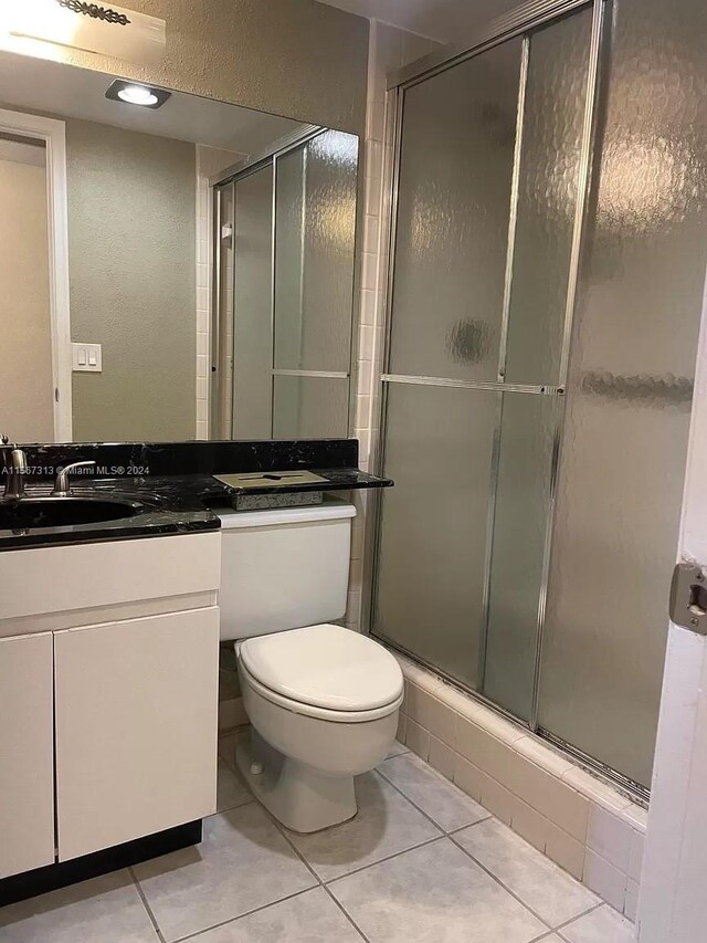 bathroom with toilet, vanity with extensive cabinet space, an enclosed shower, and tile floors