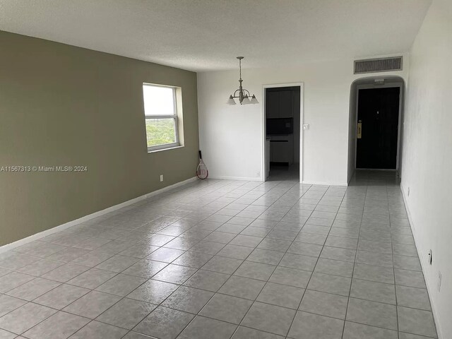 unfurnished room featuring an inviting chandelier and light tile flooring