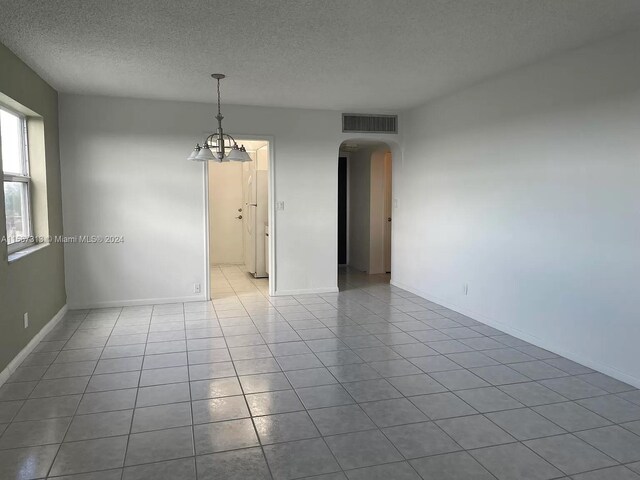 tiled empty room with a textured ceiling and a notable chandelier