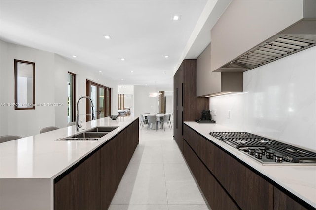 kitchen featuring custom range hood, light tile floors, sink, a kitchen island with sink, and stainless steel gas stovetop