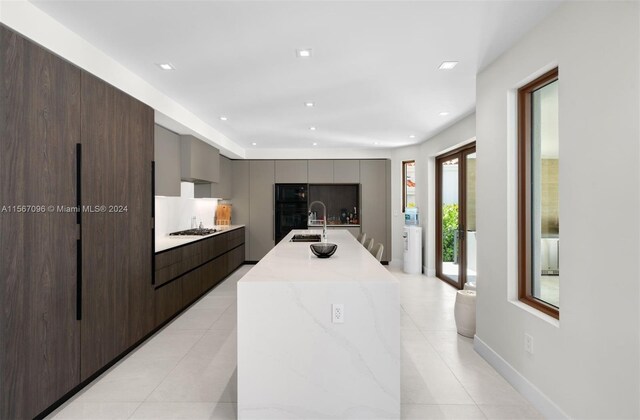 kitchen with sink, gray cabinets, an island with sink, and light tile floors