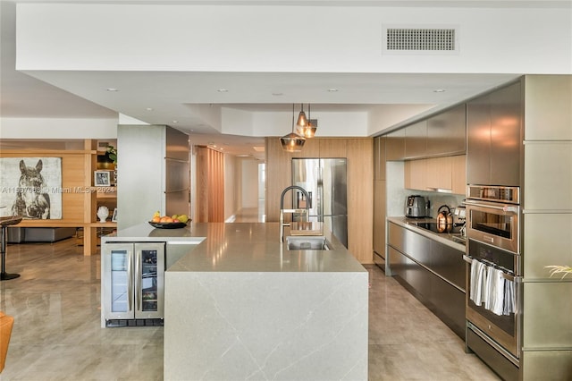 kitchen with appliances with stainless steel finishes, decorative light fixtures, sink, and an island with sink