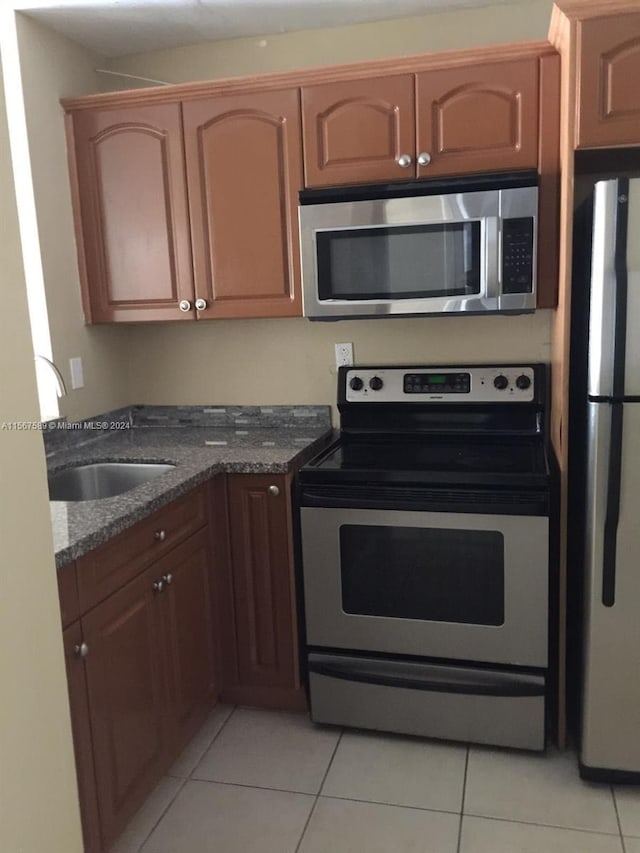 kitchen featuring dark stone counters, appliances with stainless steel finishes, light tile flooring, and sink