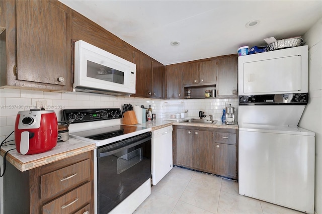 kitchen featuring tasteful backsplash, white appliances, sink, light tile patterned floors, and stacked washer and dryer