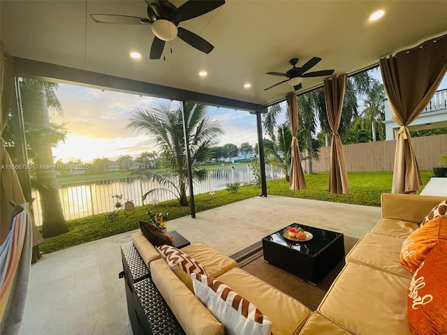 patio terrace at dusk featuring a lawn, ceiling fan, a water view, and an outdoor hangout area