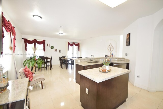 kitchen featuring sink, dark brown cabinets, light tile patterned floors, dishwasher, and a kitchen island with sink