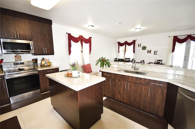 kitchen with a kitchen island, appliances with stainless steel finishes, sink, light stone counters, and dark brown cabinets