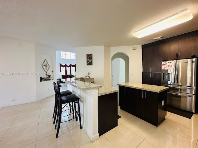 kitchen featuring a kitchen island with sink, stainless steel fridge with ice dispenser, a breakfast bar area, and light stone countertops