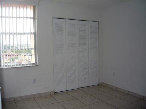 unfurnished bedroom featuring multiple windows, light tile floors, and a closet