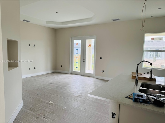 living room with a raised ceiling, light wood-type flooring, sink, and french doors