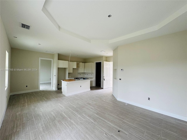 unfurnished living room with a raised ceiling, light wood-type flooring, and sink