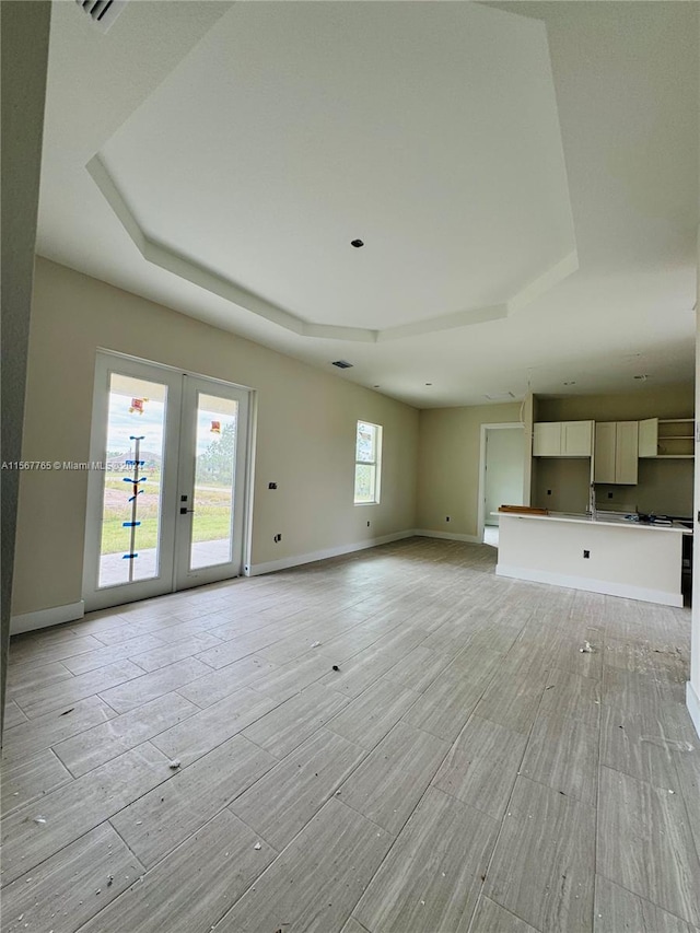 unfurnished living room with a tray ceiling, sink, french doors, and light wood-type flooring