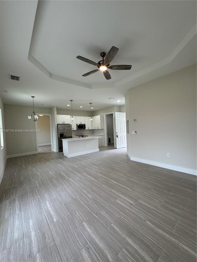 unfurnished living room with a raised ceiling and ceiling fan with notable chandelier