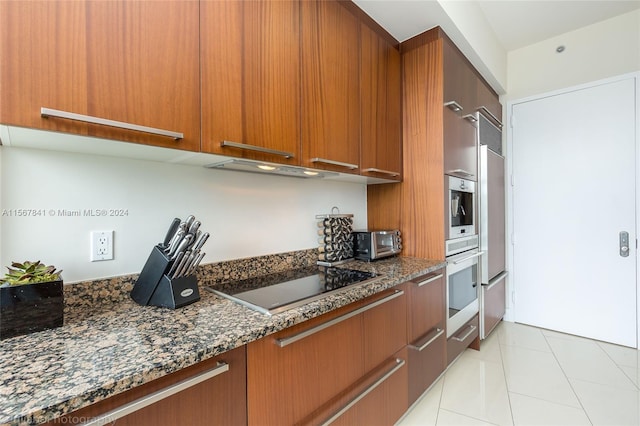 kitchen with dark stone counters, black electric stovetop, light tile floors, exhaust hood, and white oven