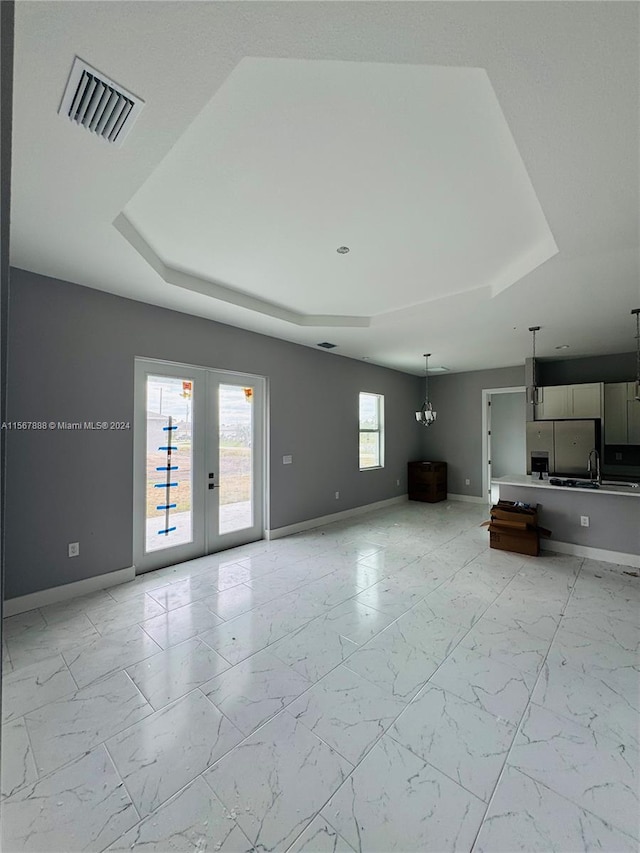 unfurnished living room with a healthy amount of sunlight, french doors, and a tray ceiling