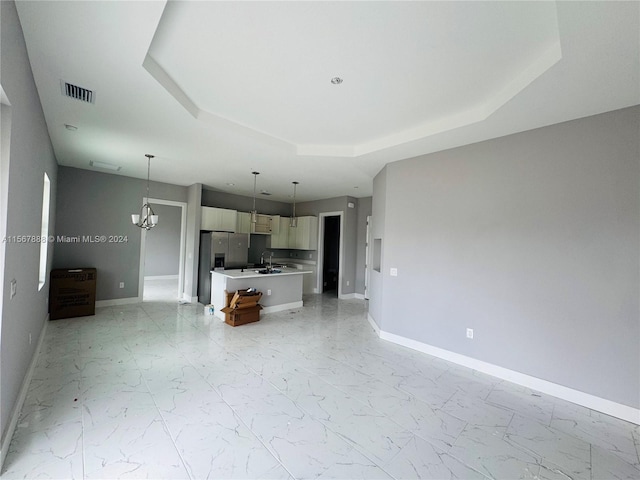 unfurnished living room featuring a tray ceiling, an inviting chandelier, and sink