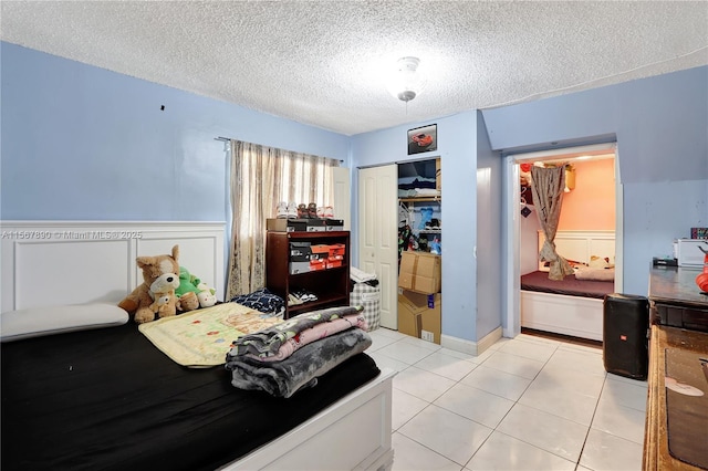 bedroom featuring light tile patterned floors, a closet, a textured ceiling, and a wainscoted wall