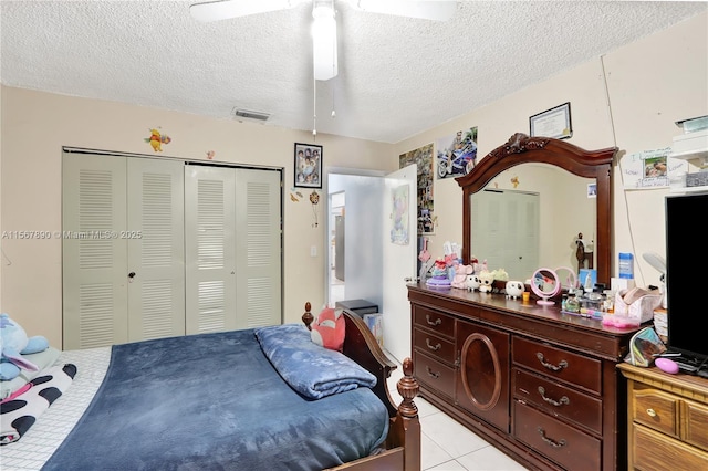 bedroom with a textured ceiling, light tile patterned floors, visible vents, a ceiling fan, and a closet