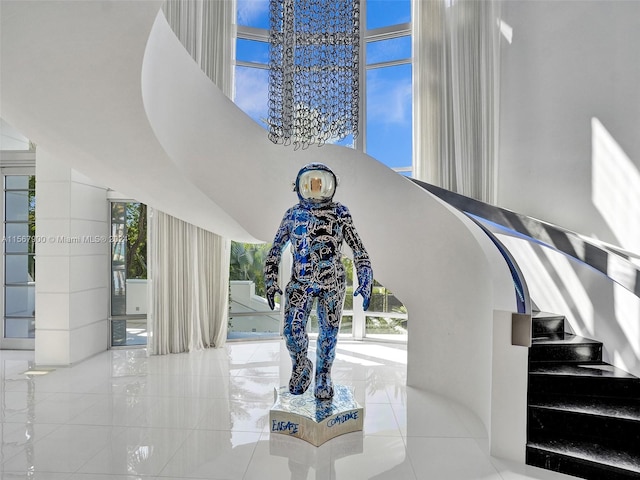 staircase with an inviting chandelier, a towering ceiling, and light tile floors