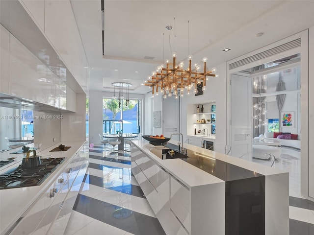 kitchen featuring gas cooktop, decorative light fixtures, an island with sink, sink, and light tile floors