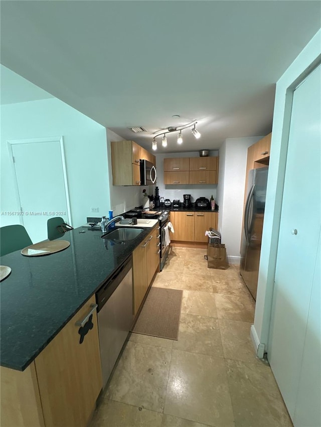 kitchen featuring light tile floors, appliances with stainless steel finishes, sink, track lighting, and dark stone counters