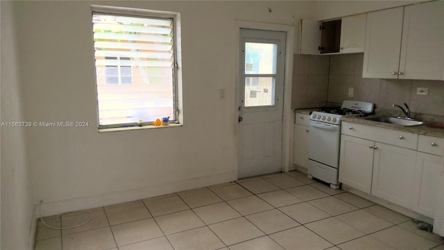 kitchen with white cabinets, light tile patterned floors, sink, and white range with gas stovetop