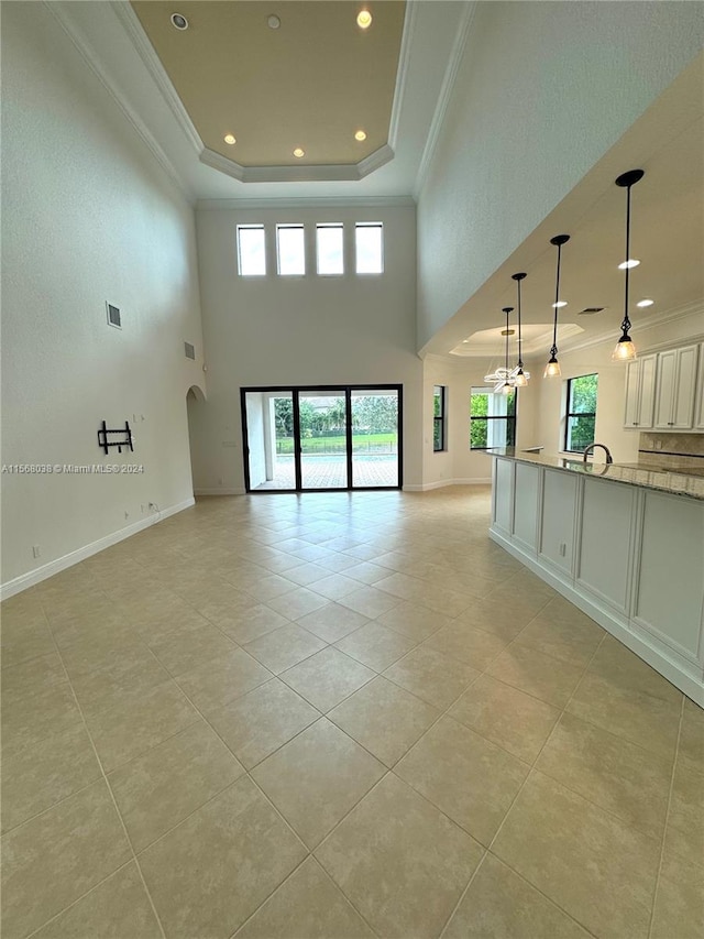 unfurnished living room with light tile patterned floors, ornamental molding, and a tray ceiling