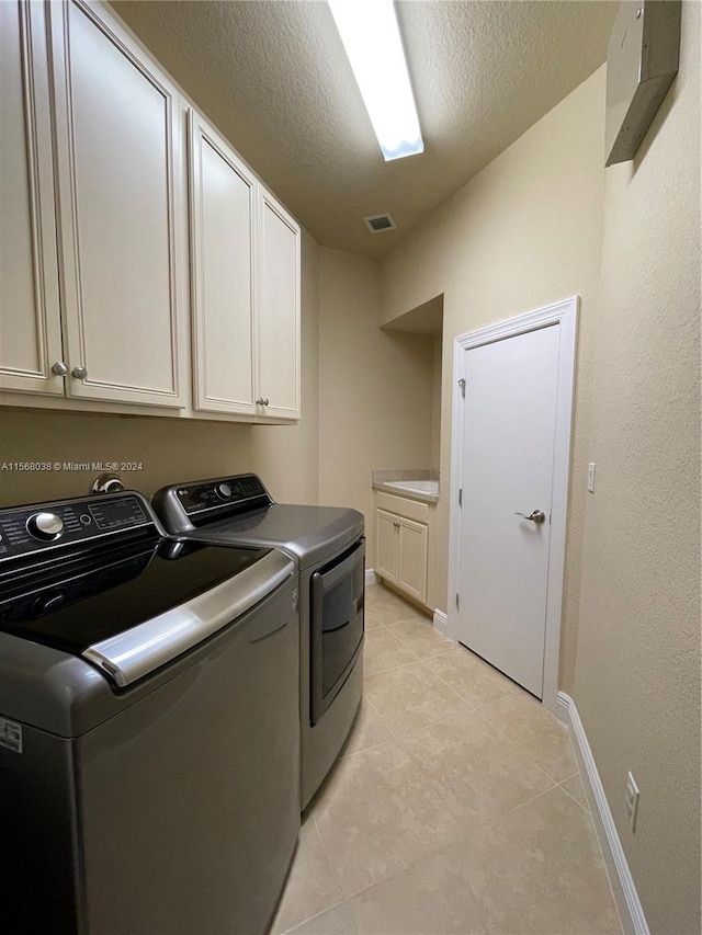 washroom featuring cabinets, light tile patterned flooring, washer and dryer, and a textured ceiling