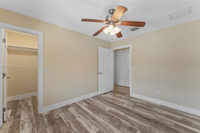 unfurnished bedroom featuring light wood-type flooring, a walk in closet, a closet, and ceiling fan