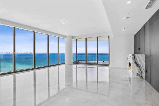 unfurnished room featuring a water view, a premium fireplace, visible vents, and a wall of windows