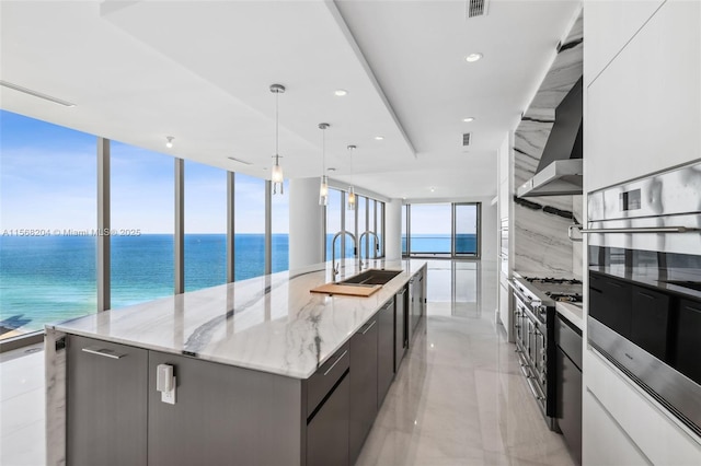 kitchen with plenty of natural light, wall chimney exhaust hood, a large island, modern cabinets, and stainless steel oven