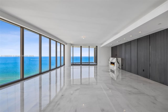 unfurnished room with a water view, a high end fireplace, and floor to ceiling windows