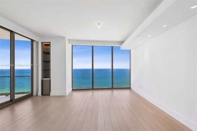 empty room featuring a water view, a wealth of natural light, a wall of windows, and hardwood / wood-style floors