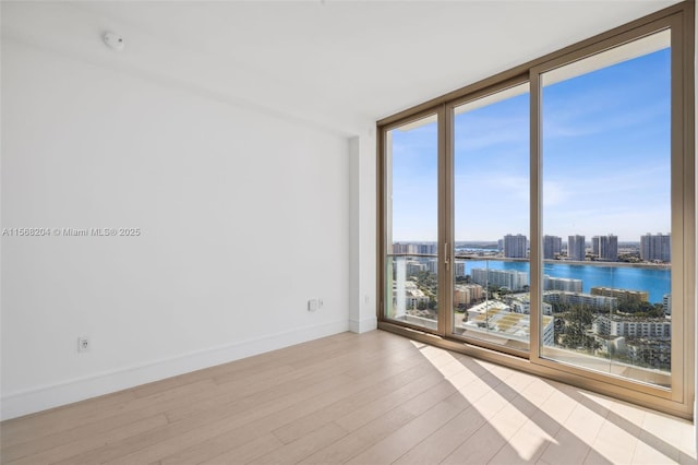 unfurnished room featuring baseboards, wood finished floors, a water view, a wall of windows, and a city view