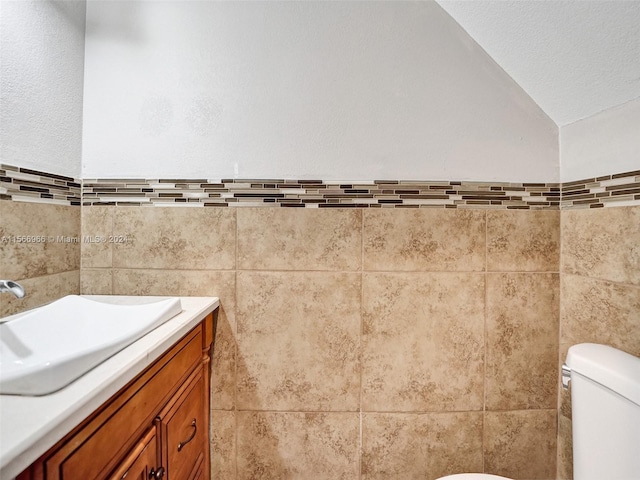 bathroom with tile walls, lofted ceiling, vanity, and toilet